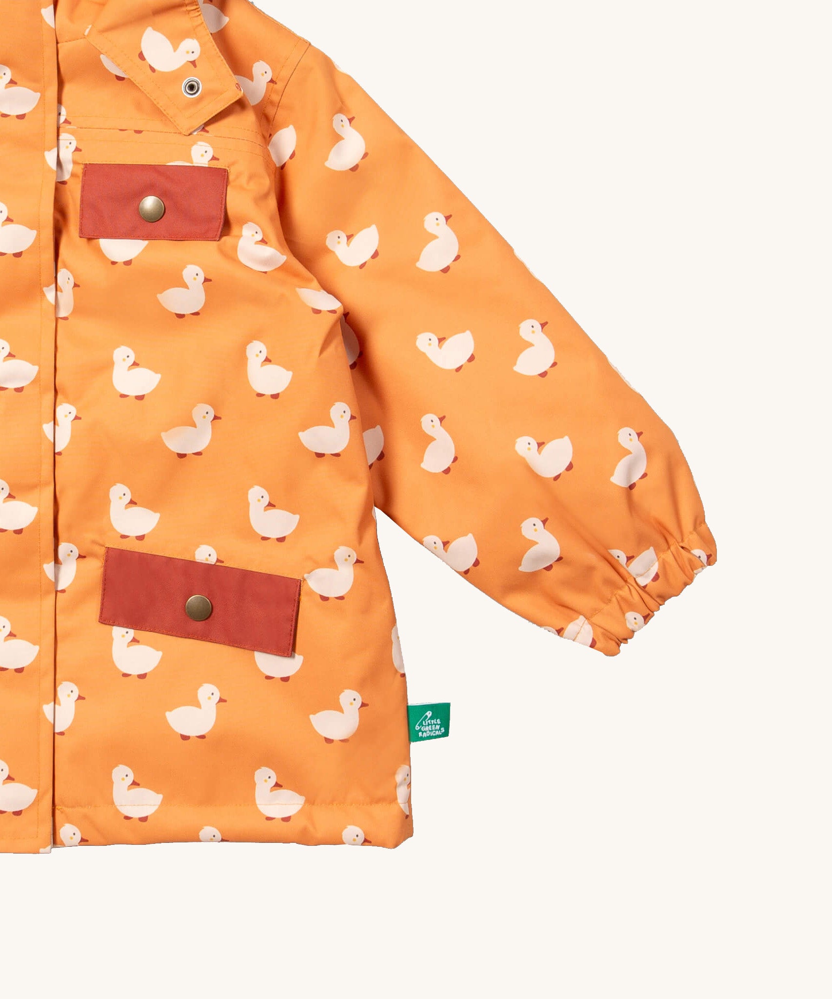 A close up of the Little Green Radicals waterproof coat in gold ducks Showing the elasticated cuff detail and red side and chest pocket on yellow recycled polyester fabric