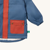 A close up of the Little Green Radicals waterproof coat in moonlight blue Showing the elasticated cuff detail and red side pocket on blue recycled polyester fabric