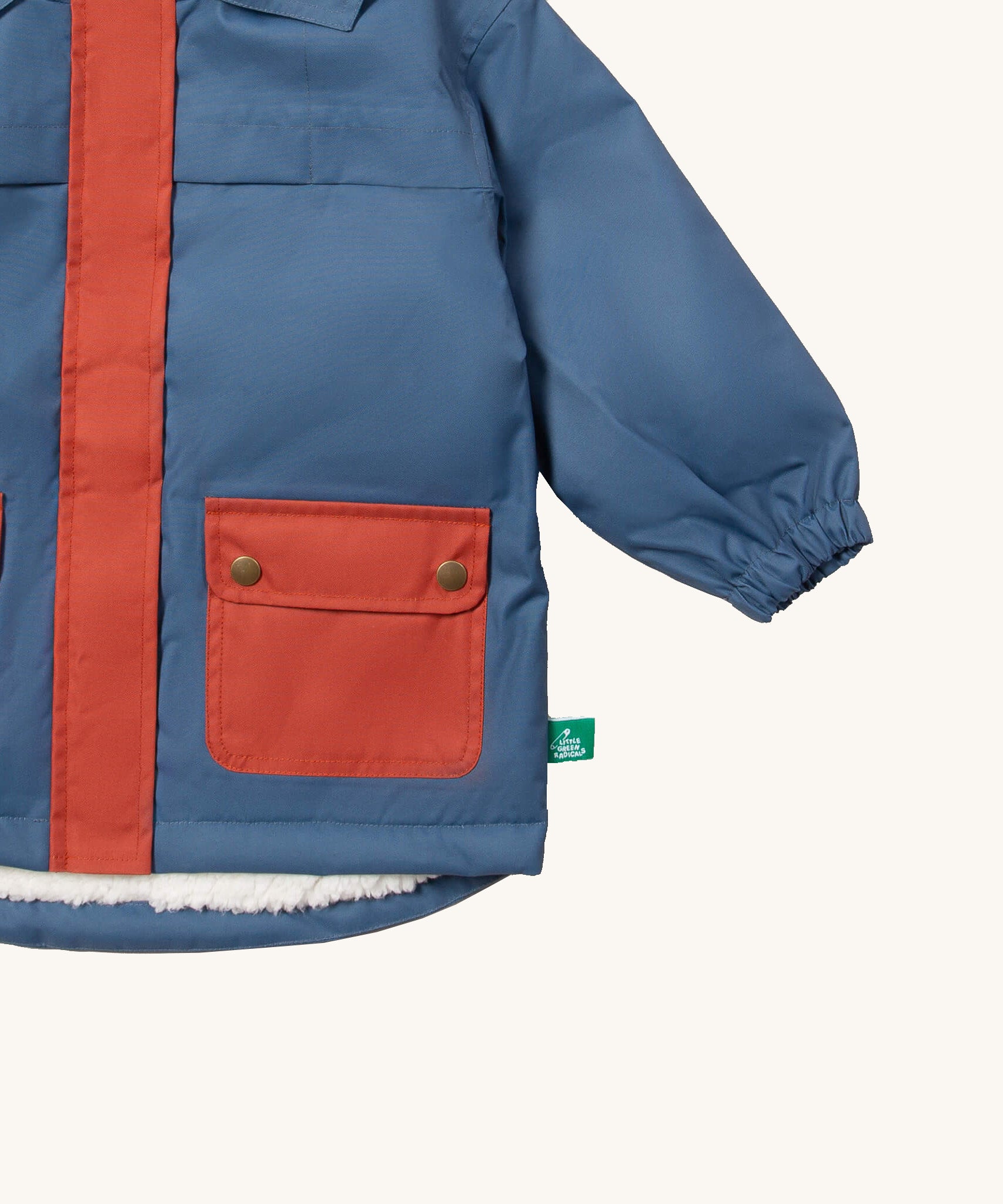 A close up of the Little Green Radicals waterproof coat in moonlight blue Showing the elasticated cuff detail and red side pocket on blue recycled polyester fabric
