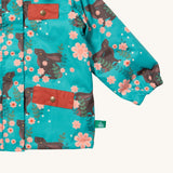 A close up of the Little Green Radicals waterproof coat in winter rabbits Showing the elasticated cuff detail and red side and chest pocket on turquoise recycled polyester fabric