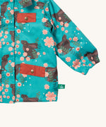 A close up of the Little Green Radicals waterproof coat in winter rabbits Showing the elasticated cuff detail and red side and chest pocket on turquoise recycled polyester fabric