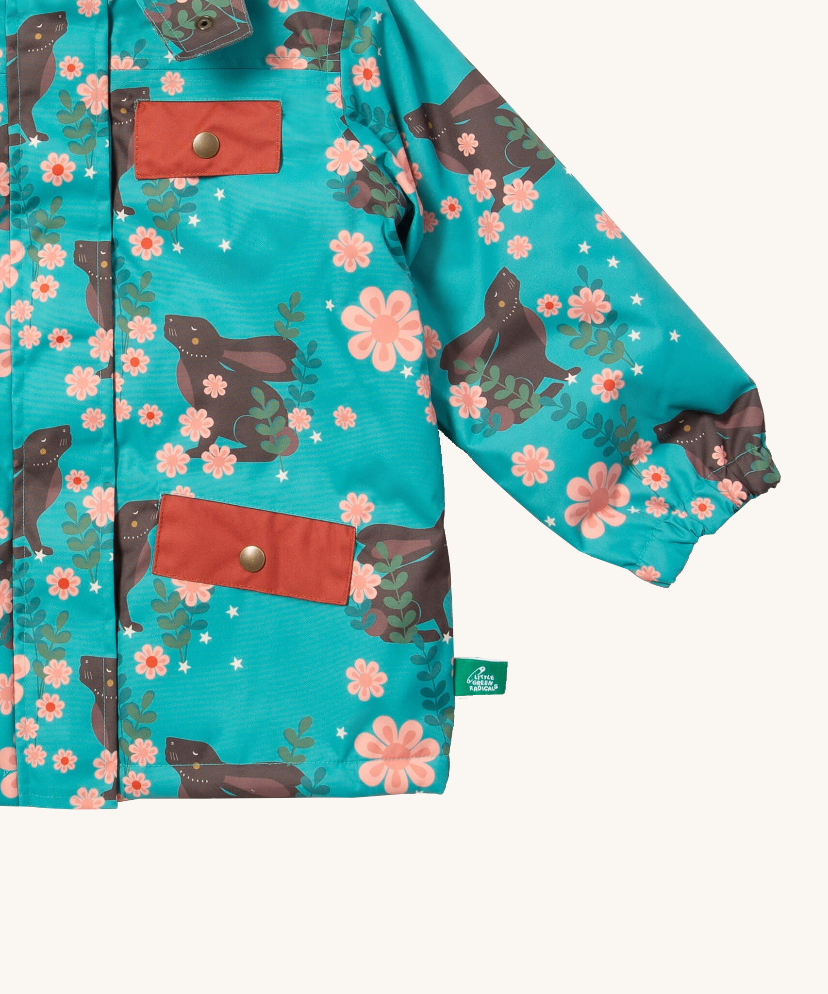 A close up of the Little Green Radicals waterproof coat in winter rabbits Showing the elasticated cuff detail and red side and chest pocket on turquoise recycled polyester fabric