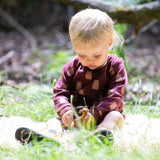 A young child sitting on grass wearing a Little Green Radicals Baby Bodysuit 2 Pack featuring a Brown Bears print. Little Green Radicals offer a range of organic cotton children's clothing available here at Babipur.