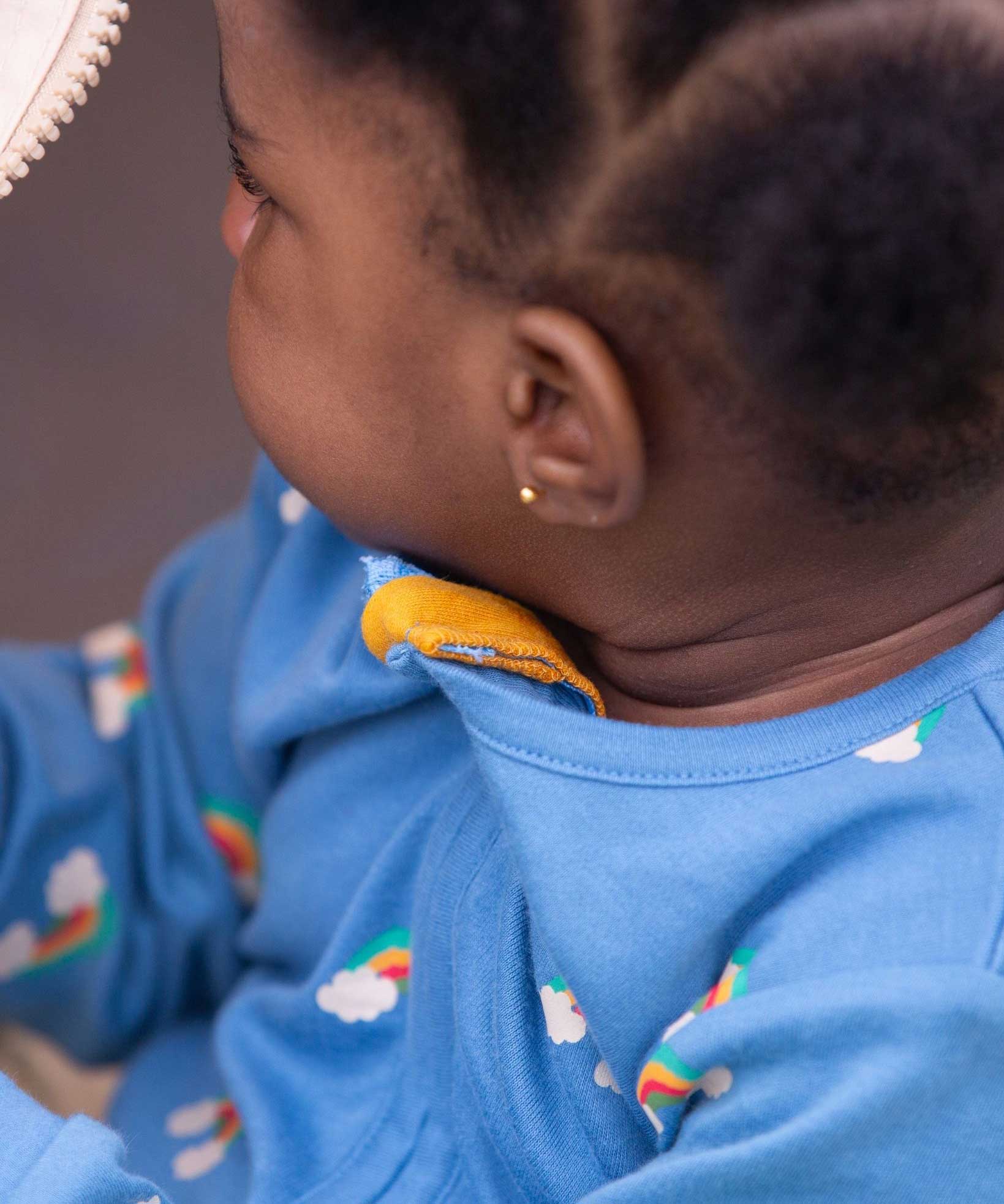 A close up of a baby wearing the Little Green Radicals Blue Rainbows Zip Organic Babygrow. The close up shows the yellow coloured cotton zip guard on the neck of the babygrow. Little green Radicals have a wide range of organic cotton, Fairtrade clothing and outerwear for babies and children available here at Babipur.