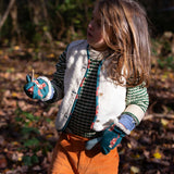 A child wearing the Little Green Radicals fox print sherpa fleece lined mittens with a knitted jumper and sherpa lined reversible gilet and yellow corduroy trousers. The children's sized mittens are part of a wide range of organic cotton clothing for children available here at Babipur.