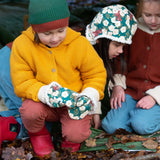 A child wearing the  Little Green Radicals Hedgerow print Children's Sherpa Lined Mittens with a yellow gold knitted cardigan and ginger orange corduroy trousers. There is a child in the background wearing a hedgerow sherpa lined hat.