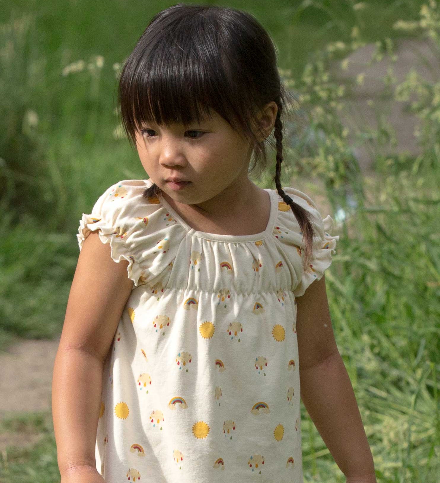 A close up of a A child wearing the Little Green Radicals Sunshine & Rainbows Pocket Playdays Dress. Little green Radicals have a wide range of organic cotton, Fairtrade children's clothing and outerwear available here at Babipur.