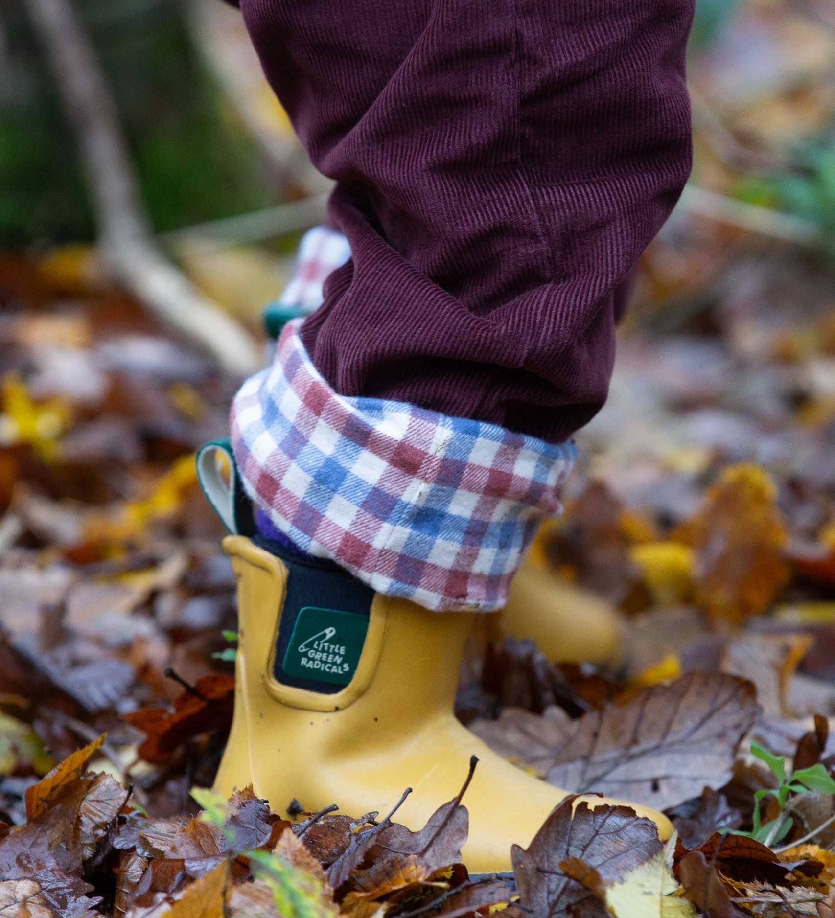 A close up of a child wearing the Little Green Radicals Chocolate brown Cord Lined Trousers with yellow gold wellington boots. These trousers are part of a wide range of organic cotton clothing for children available here at Babipur.