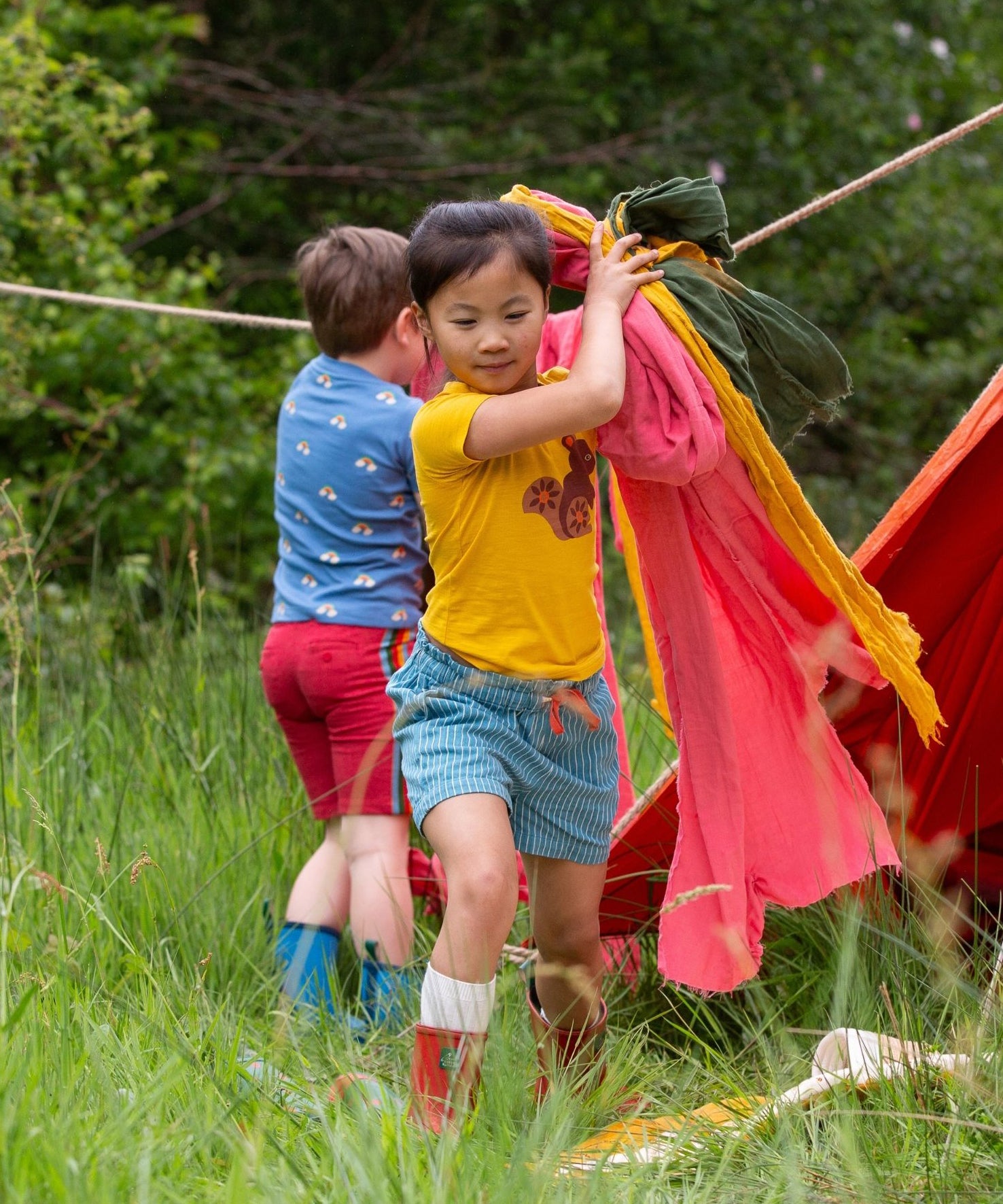 A child wearing the Little Green Radicals Yellow gold coloured Squirrel t-shirt with blue striped shorts.