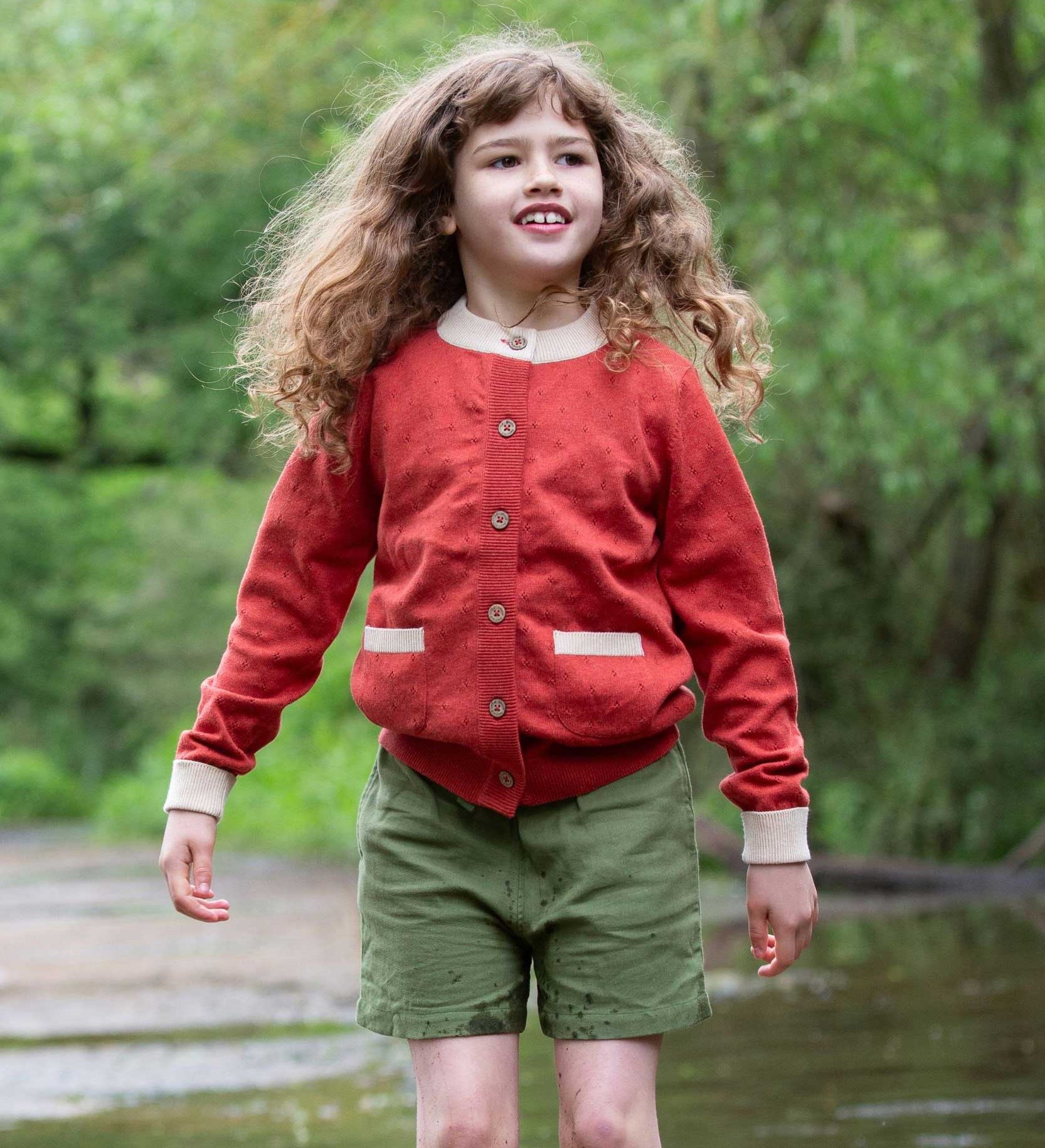 A child wearing a Little Green Radicals From One To Another Burnt Ochre Pointelle Knitted Cardigan with green coloured shorts. Little green Radicals have a wide range of organic cotton, Fairtrade children's clothing and outerwear available here at Babipur.