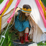 A child wearing the Little Green Radicals Child's Organic Cotton Horizon Blue Striped Pinafore Button Dress with red wellington boots and a knitted yellow gold coloured crown.
