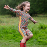 A child wearing the Little Green Radicals Vintage Flowers UPF 50+ Recycled Sunsafe Sunsuit with a pair of red wellington boots.