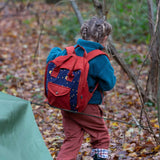 A child walking through a forest wearing the Little Green Radicals dark nights corduroy backpack on their back. A 100% organic cotton backpack in a navy and red corduroy style with a starry night design. Features a handle on the top for easy carrying a front pocket and 2 bottle holders. This children's bag is a part of a wide range of organic cotton clothing and accessories for children available here at Babipur.
