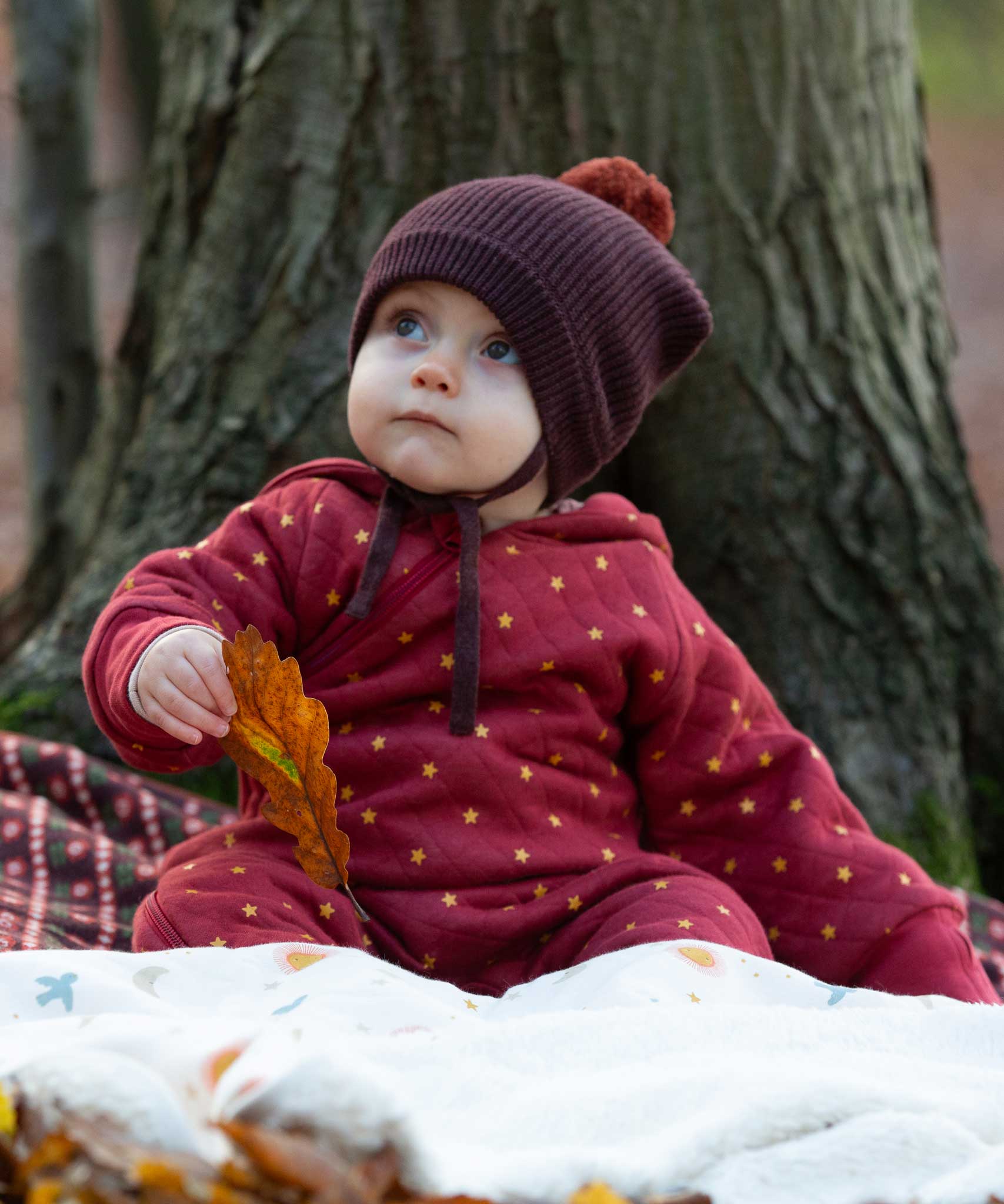 A baby wearing the Little Green Radicals Organic Cotton Quilted Snug Suit with a Red Stars design. This snug suit is a part of a wide range of organic cotton clothing for children available here at Babipur.