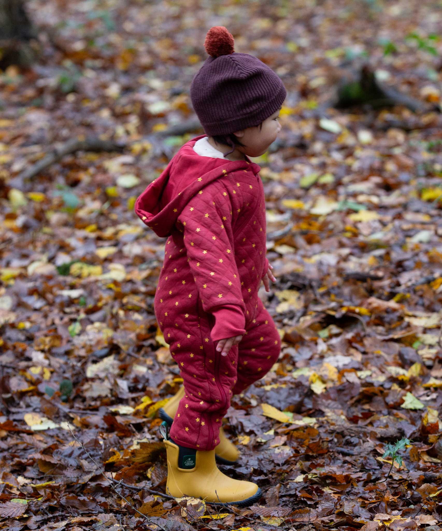 A child wearing the Little Green Radicals Organic Cotton Quilted Snug Suit with a Red Stars design. This snug suit is a part of a wide range of organic cotton clothing for children available here at Babipur.