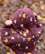 A close up of the hood with a child wearing the Little Green Radicals Organic Cotton Flying Birds Quilted Snug Suit. A maroon brown coloured suit with an all over print featuring flying birds, stars, moon and  sun. This snug suit is a part of a wide range of organic cotton clothing for children available here at Babipur.
