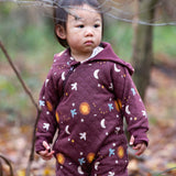 A child wearing the Little Green Radicals Organic Cotton Flying Birds Quilted Snug Suit. A maroon brown coloured suit with an all over print featuring flying birds, stars, moon and  sun. This snug suit is a part of a wide range of organic cotton clothing for children available here at Babipur.