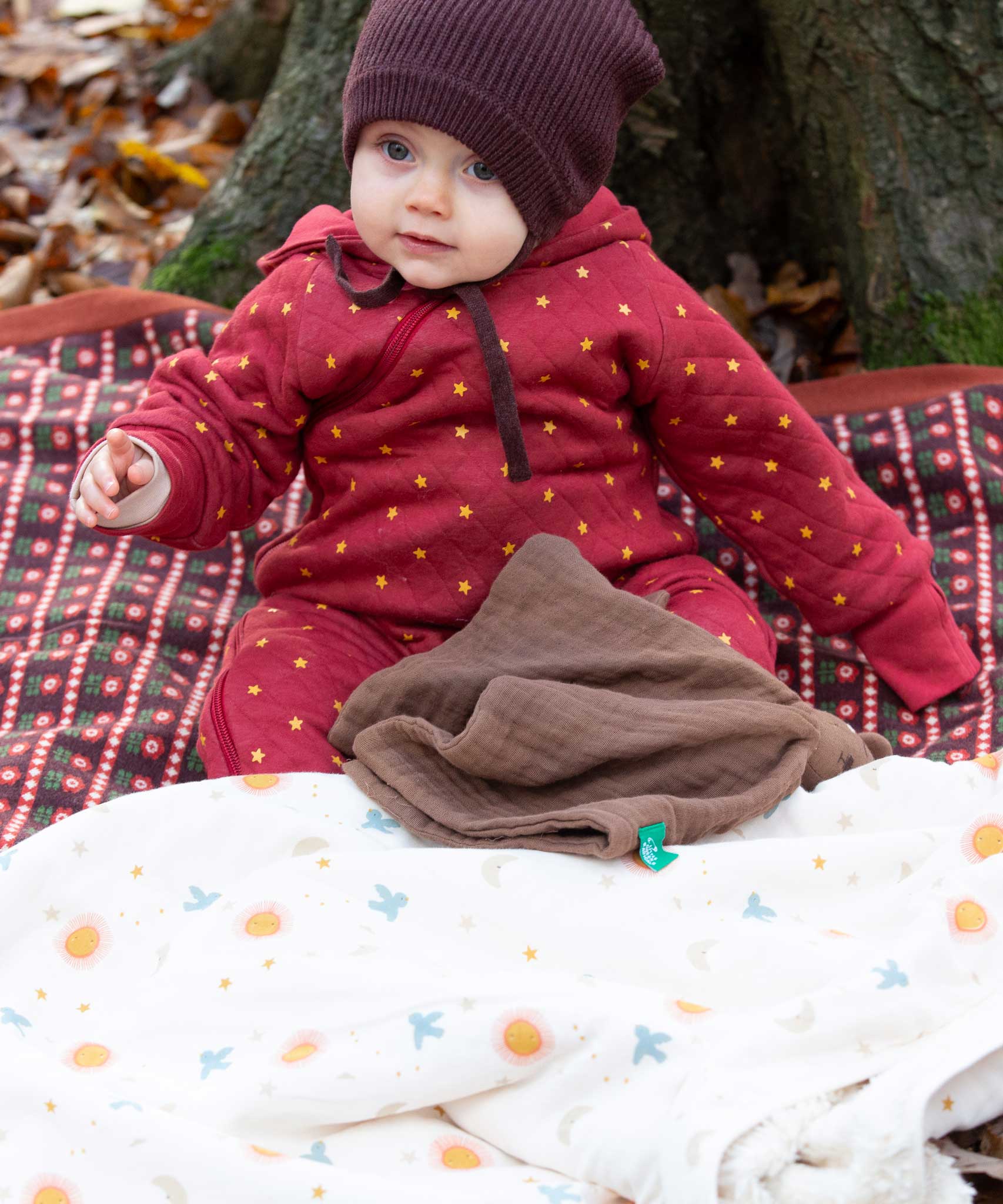 A baby wearing the Little Green Radicals Organic Cotton Quilted Snug Suit with a Red Stars design. This snug suit is a part of a wide range of organic cotton clothing for children available here at Babipur.
