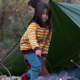 A child standing by a campfire in the forest, wearing the Little Green Radicals Reversible Easy Rider Jacket on the Brown Bears print side. Little green Radicals have a wide range of organic cotton, Fairtrade children's clothing an outerwear available here at Babipur.