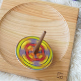 A Mader coloured disc placed on the so and so spinner. The spinner can be seen spinning in motion on a wooden spinning plate.