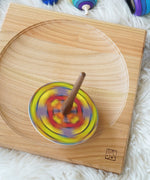 A Mader coloured disc placed on the so and so spinner. The spinner can be seen spinning in motion on a wooden spinning plate.