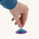 A wooden purple and blue flamenco Mader spinning top held by a hand on a cream background.