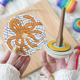 A Mader o and So wooden spinner being held up next to the octopus print cardboard disc.