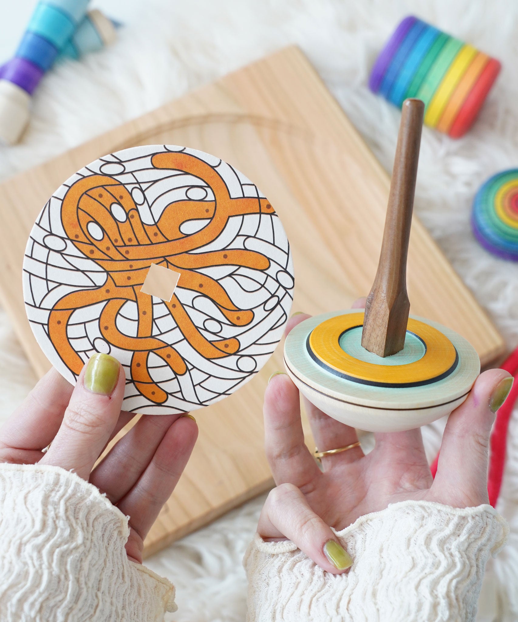 A Mader o and So wooden spinner being held up next to the octopus print cardboard disc.
