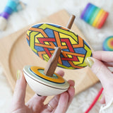 A cardboard disc being placed in the Mader So and So wooden spinning top set.