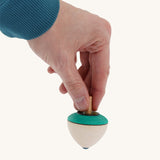 A wooden flower egg Mader spinning top held by a hand on a cream background.