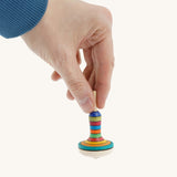 A wooden manolette spinning top held by a hand on a cream background.