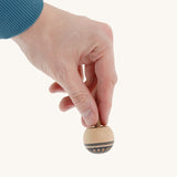 A wooden Mader Oriental spinning top held by a hand on a cream background.
