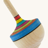A wooden Mader traditional rainbow spinning top on a cream background.