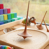 Mader wooden Trumpo spinning top on a Mader spinning plate surrounded by wooden spinning tops and a Grimms Large Stepped Pyramid