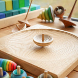 Mader wooden UFO spinning top on a Mader spinning plate surrounded by wooden spinning tops and a Grimms Large Stepped Pyramid