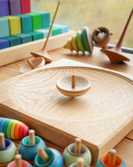 Mader wooden UFO spinning top on a Mader spinning plate surrounded by wooden spinning tops and a Grimms Large Stepped Pyramid
