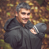 Mamalila Shelter Men's Babywearing Rain Jacket in Anthracite. Lifestyle view of this men's technical babywearing rain coat with the baby carrier insert on the front. Woodland background