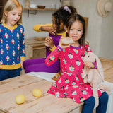 A child wearing the Maxomorra Fairy print circle dress. The child is sitting on a kitchen counter top. Other children can be seen in the background.