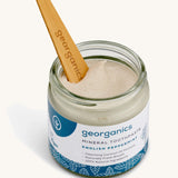 A opened jar of the Georganics english peppermint mineral toothpaste with the tongue stick dipped in