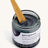An opened jar of mineral activated charcoal toothpaste with the tongue stick dipped in
