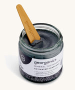 An opened jar of mineral activated charcoal toothpaste with the tongue stick dipped in