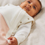 A close up of a baby laid on a soft surface inside the blush stripe MORI swaddle. Showing the popper detail on the arms, and design detail