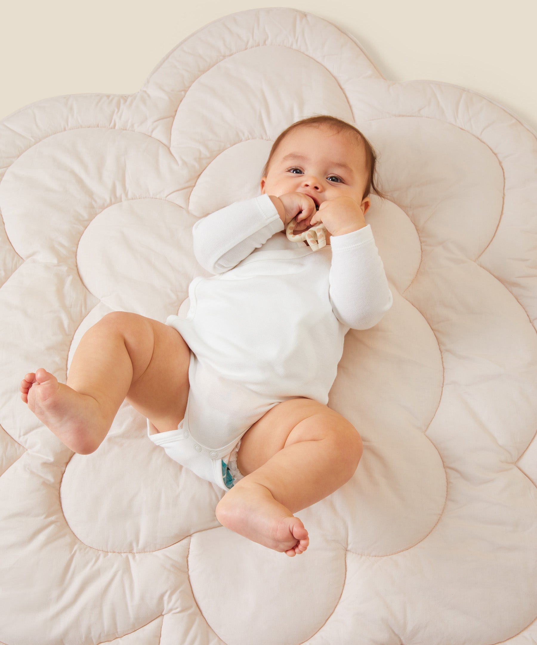 A little baby laying on a flower-shaped mat, wearing the Mori organic kimono baby bodysuit in white.