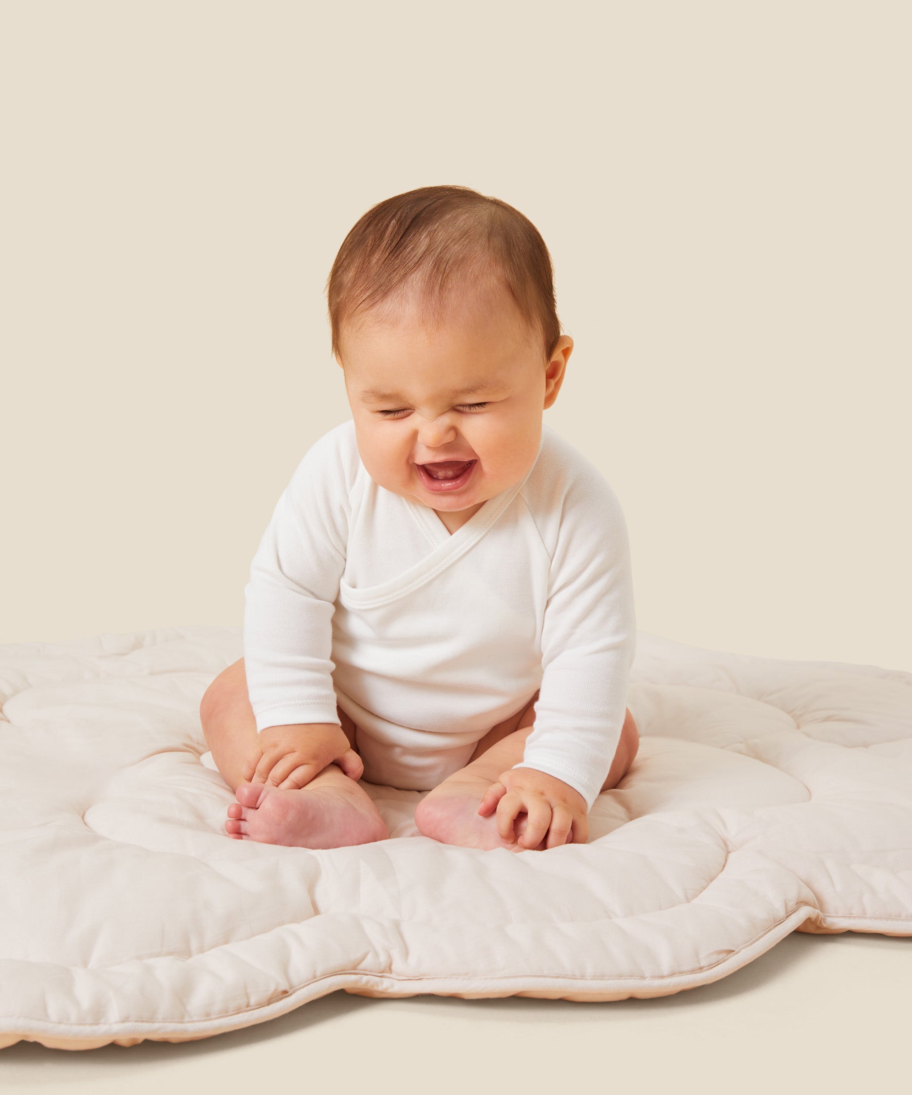 A baby sitting up and laughing, wearing the Mori organic kimono baby bodysuit in white.
