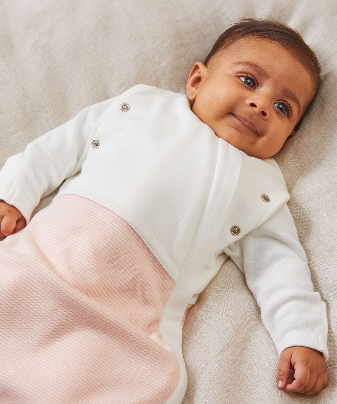 A close up of the MORI blush stripe baby swaddle showing the popper detail on the arms, to tuck the arms in or let them be free.
