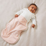 A baby laid on a soft surface inside the blush stripe MORI swaddle. Made from bamboo and organic cotton and features poppers on the arms, to tuck the arms in or let them be free.