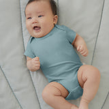 A baby wearing a sky blue Mori organic cotton baby bodysuit with short sleeves.