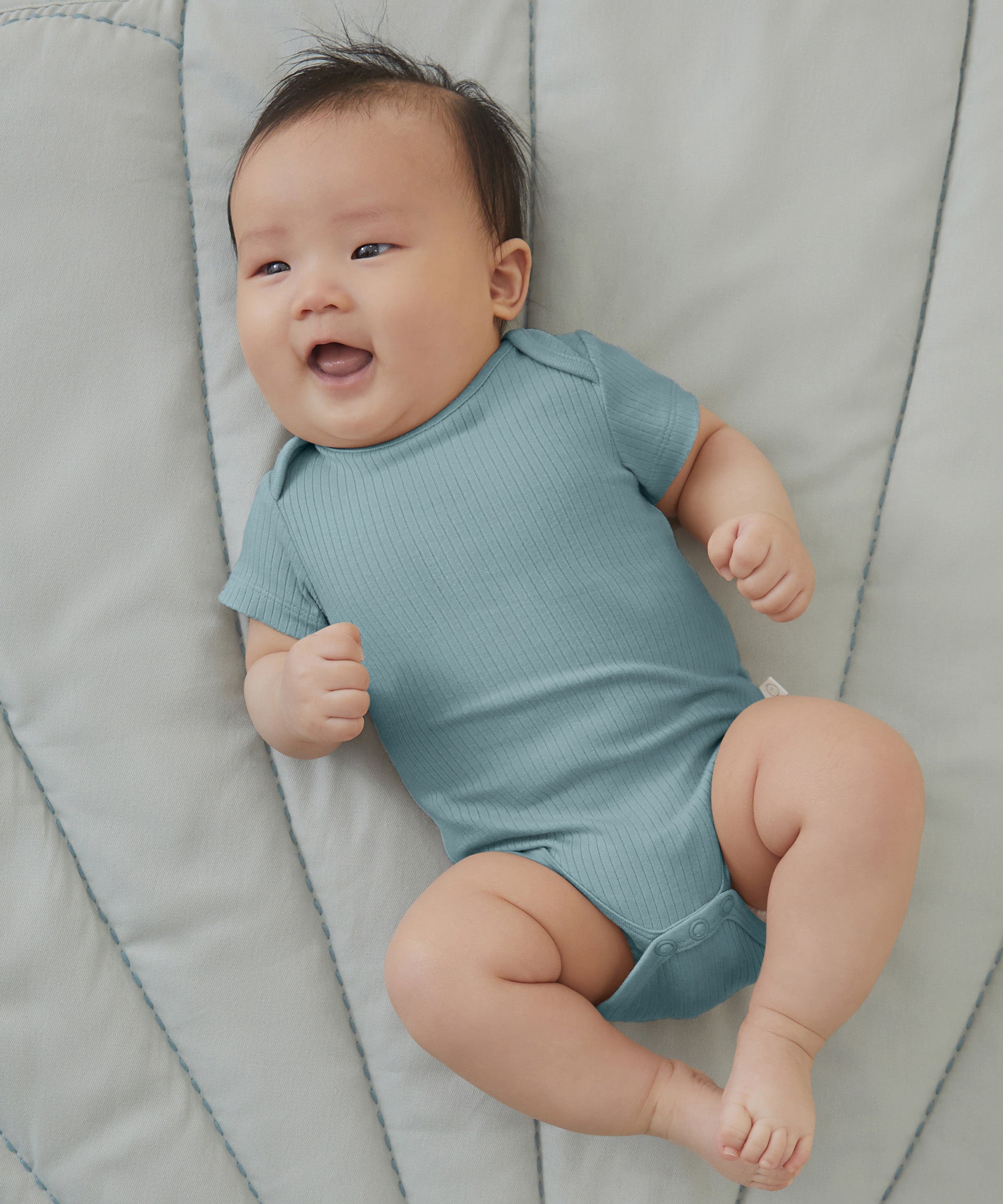 A baby wearing a sky blue Mori organic cotton baby bodysuit with short sleeves.