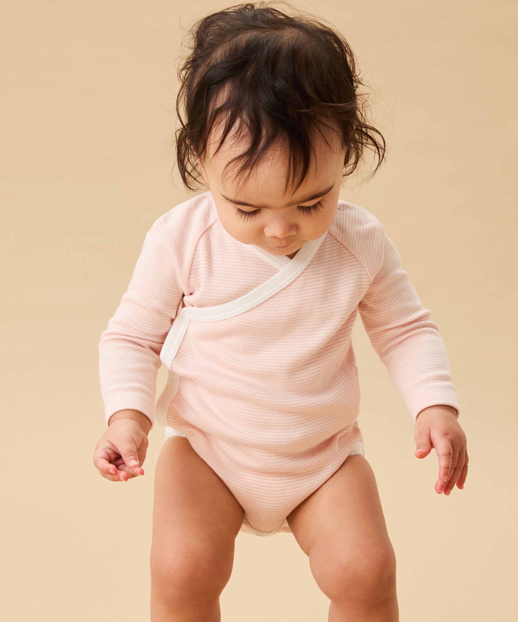 A toddler standing up, and wearing the Mori organic cotton and bamboo blend baby kimono bodysuit in a pink blush stripe design.