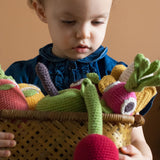 Girl holding a basket full of Myum handmade crochet soft vegetable toys in front of a beige wall